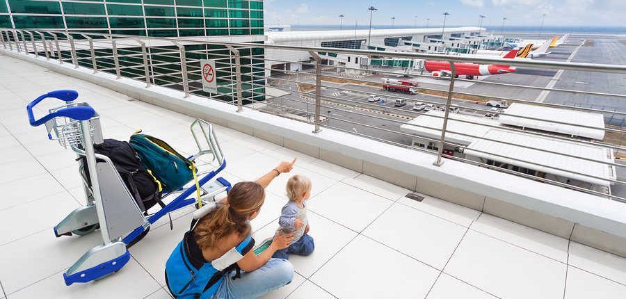 mujer con bebe en aeropuerto mirando los aviones con carrito de maletas