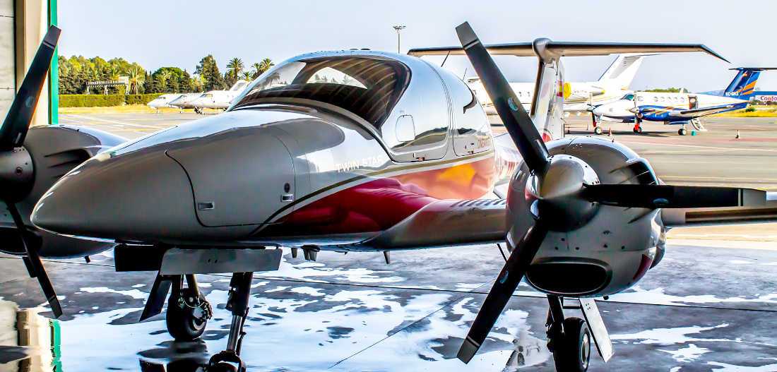 vista frontal de aeronave diamond da42 de one air en hangar con aviones al fondo