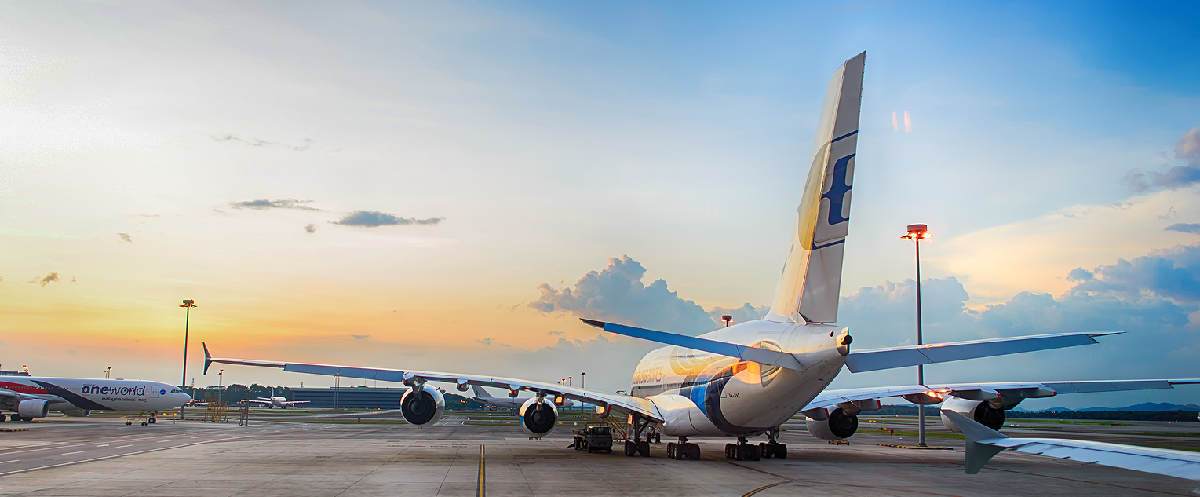 trasera de avion de pasajeros parado en pista de aeropuerto con cielo azul y naranja