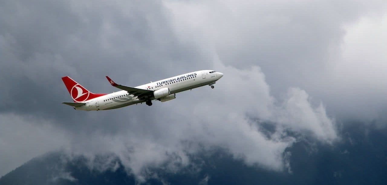 avion de la aerolinea turkish airlines sobrevolando una montaña rodeada de nubes