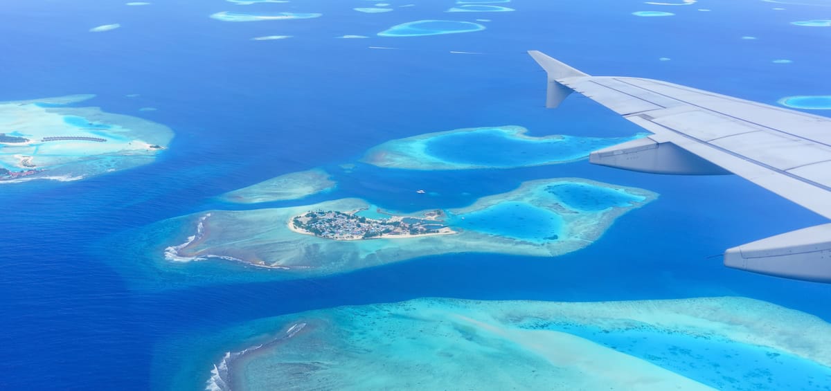 vista aerea de isla en el oceano desde ventanilla de avion con ala y motores a un lado