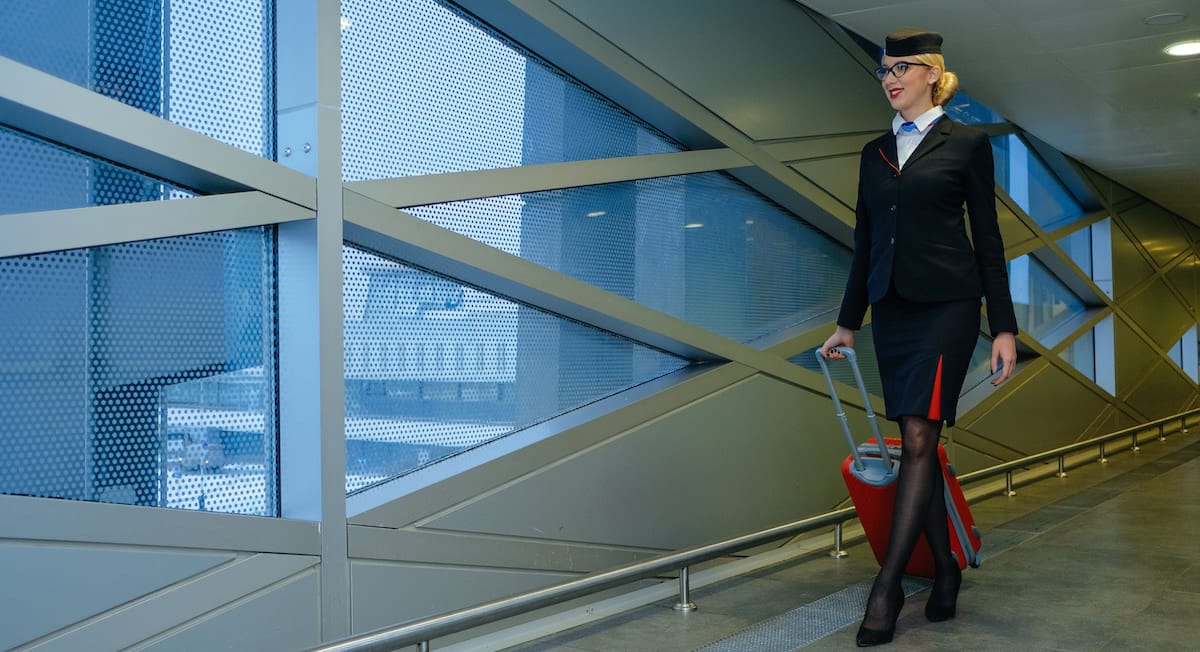 auxiliar de vuelo con uniforme y maleta llegando a aeropuerto despues de un vuelo