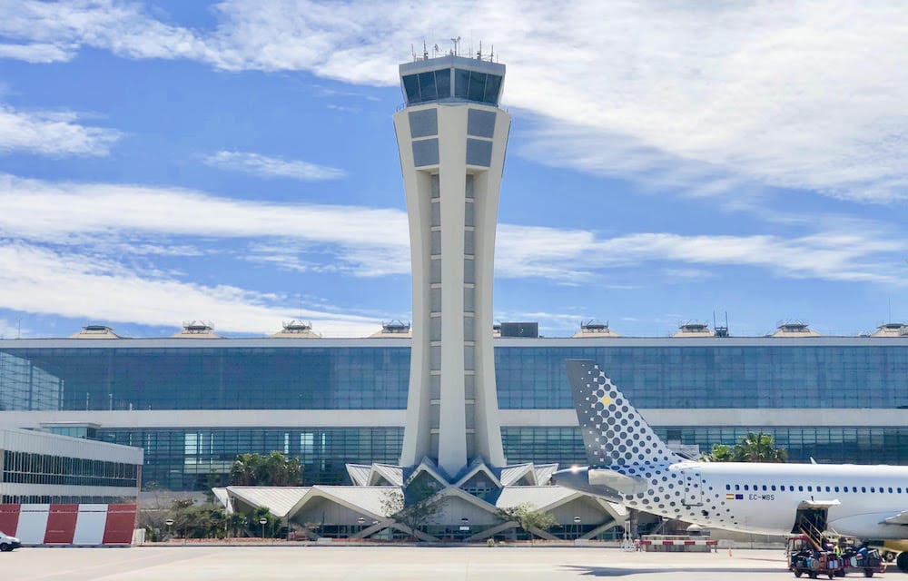 Vista exterior de la torre de control del Aeropuerto de Málaga (AGP) con avión comercial a un lado.